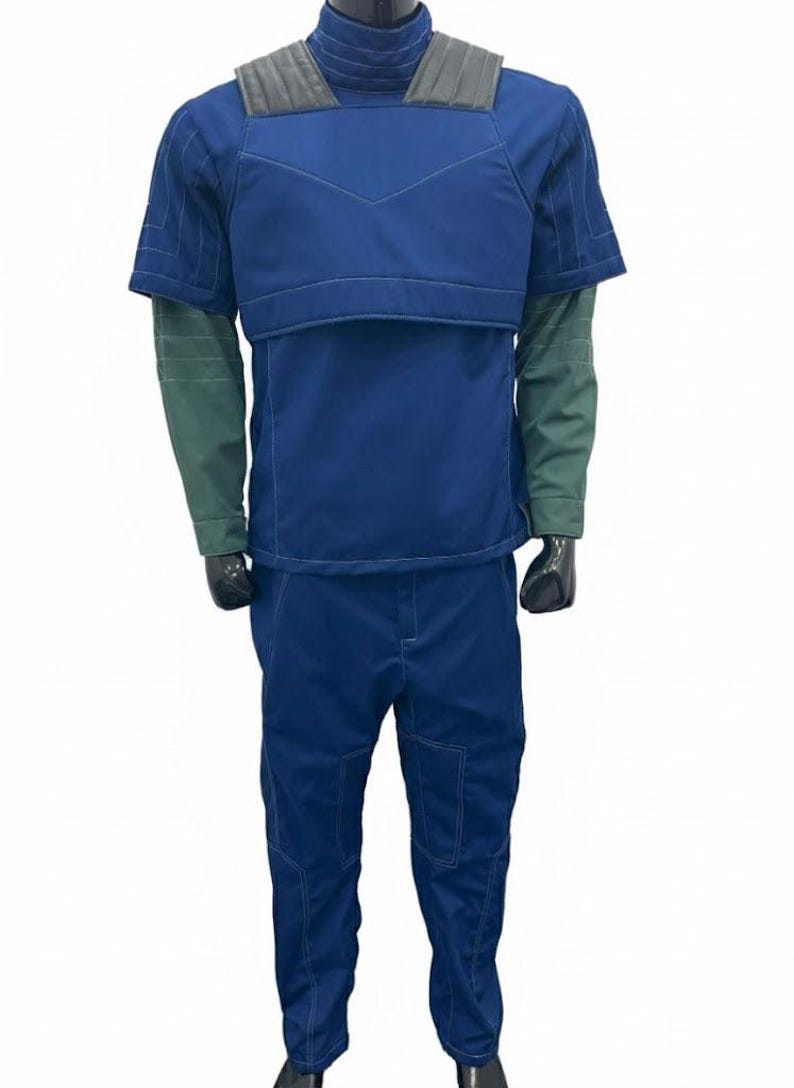 May include: A blue jumpsuit with a short-sleeved top and matching pants. The top has a padded chest and shoulder area with a gray collar. The sleeves are green. The pants have pockets and visible stitching. The outfit is displayed on a mannequin.