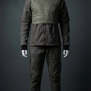 May include: A full-body outfit on a mannequin. The ensemble includes a jacket with a green chest panel, matching pants, and a high-neck collar. The outfit is a muted brown color with black cuffs.