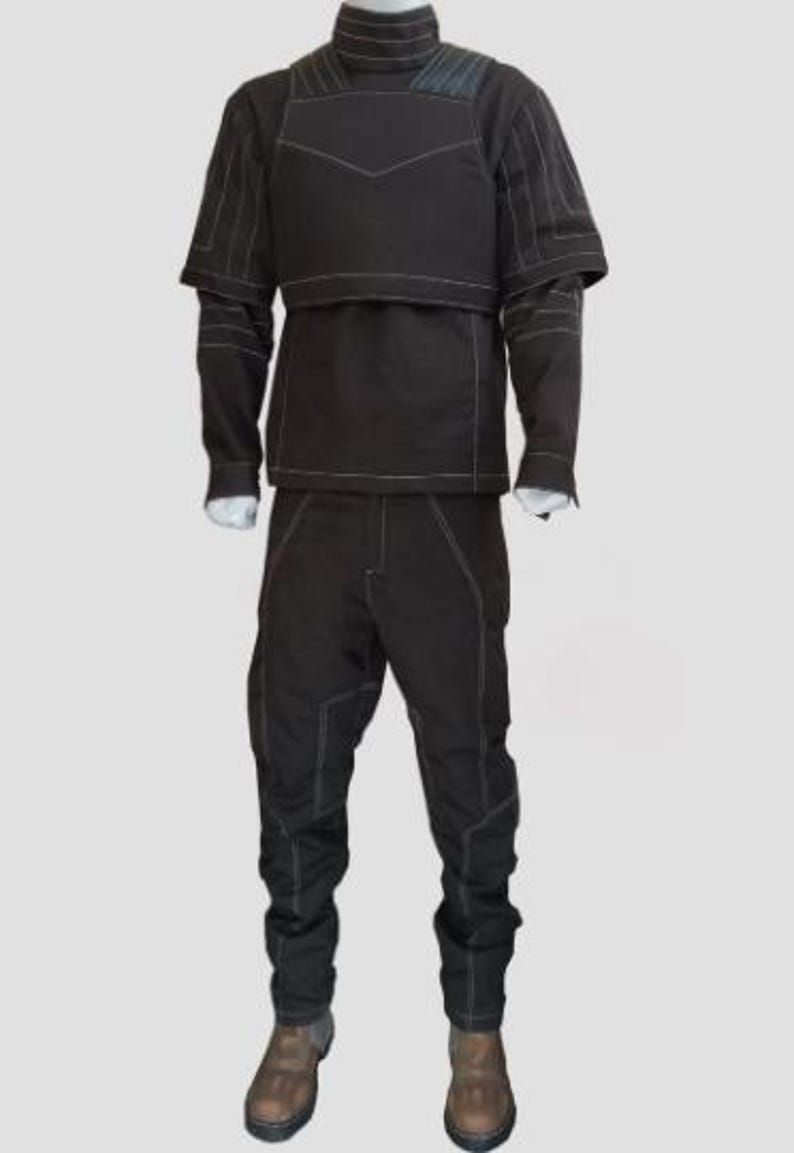 May include: A dark brown tactical suit with white stitching details. The outfit includes a high-neck jacket with a chest panel and long sleeves, and matching pants. The suit is displayed on a mannequin, showcasing its design and construction.