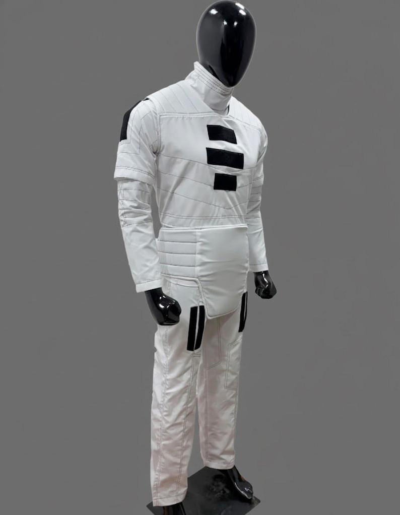 Op de afbeelding: Een witte jumpsuit met zwarte accenten, getoond op een mannequin. De outfit heeft een hoge kraag, horizontale zwarte strepen op de borst en zwarte details op de schouders en benen. De mannequin heeft een zwarte kop en handschoenen.