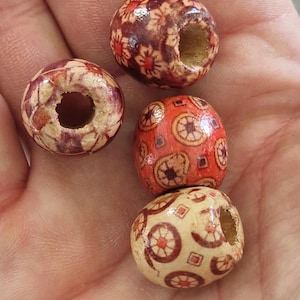 Può includere: Quattro perline di legno rotonde con un foro centrale, ognuna caratterizzata da un motivo stampato distinto. I disegni includono motivi floreali, forme geometriche e schemi circolari in tonalità rosso scuro, arancione e crema, con finitura lucida.