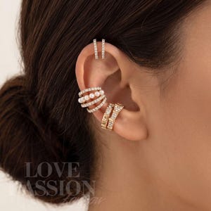 May include: A set of gold-toned ear cuffs featuring two thin upper cuffs with clear stones, a multi-band cuff with white pearls and clear stones, and a wider lower cuff with clear stones. The text LOVE PASSION is visible in the lower left corner.