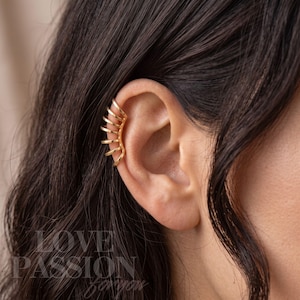 May include: A gold-toned ear cuff featuring a series of five parallel, curved wire bands that wrap around the outer edge of the ear cartilage. The piece has a polished metallic finish and is positioned securely along the upper ear rim.