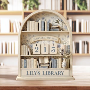 May include: A decorative arched wooden bookshelf display featuring miniature books, a small lamp, and a vase with dried flowers. The center displays the text BOOKS READ THIS YEAR above a three-digit counter showing 215 and LILY'S LIBRARY at the base.