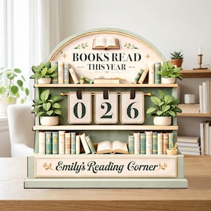 以下が含まれることがあります： 「BOOKS READ THIS YEAR」と「Emily's Reading Corner」の文字が入った装飾的な本棚。 「026」を表示するカウンターがあり、ミニチュアの本と鉢植えの植物で飾られています。 配色は主に緑とクリーム色です。
