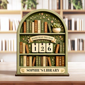 May include: A wooden bookshelf-shaped display with the text "BOOKS READ THIS YEAR" and "126". The display is painted green and decorated with floral accents and miniature book replicas. The bottom of the display reads "SOPHIE'S LIBRARY".