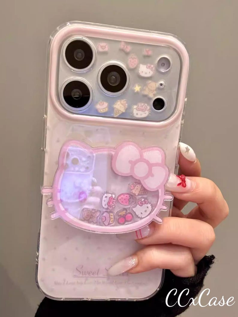 May include: A clear and pink phone case featuring a Hello Kitty design with a bow. The case has a clear back with floating charms and a pink border. The text "Sweet" is visible on the case.