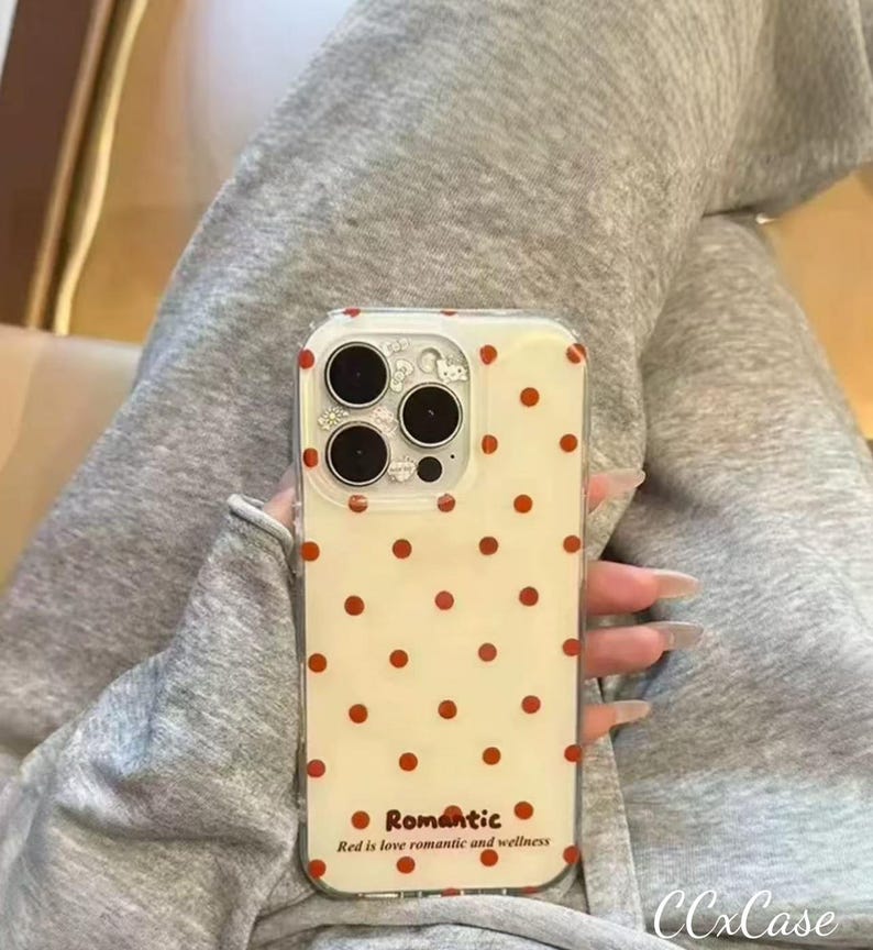 Puede incluir: Una funda transparente para tel&eacute;fono con fondo color crema y un patr&oacute;n de lunares rojos espaciados. La funda tiene un recorte para la c&aacute;mara y la palabra "Romantic" con el texto "Red is love romantic and wellness" impreso en la parte inferior.