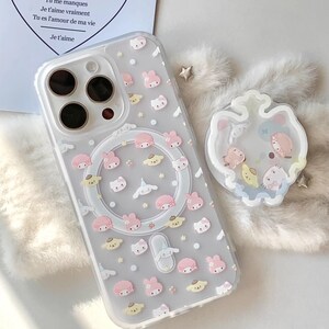 May include: Clear phone case with a pattern of pink, yellow, and white cartoon characters. The case has a magnetic ring and a clear border. The text "Je t'aime" is visible on a card in the background. The brand name "CCxCase" is at the bottom.