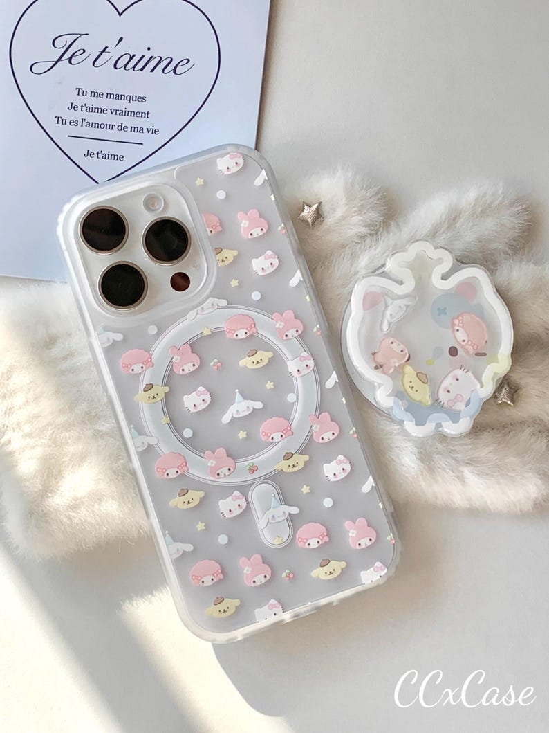May include: Clear phone case with a pattern of pink, yellow, and white cartoon characters. The case has a magnetic ring and a clear border. The text "Je t'aime" is visible on a card in the background. The brand name "CCxCase" is at the bottom.