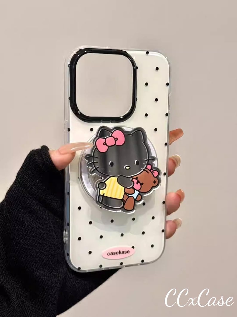 May include: Clear phone case with black polka dots and a black border. The case features a black Hello Kitty design with a pink bow and a brown teddy bear. The text "casekase" is printed on the bottom.