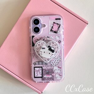 Op de afbeelding: Transparante telefoonhoes met een roze achtergrond, met een hartvormige popsocket met een Hello Kitty-ontwerp. De hoes heeft een collage van roze en zwarte patronen, waaronder luipaardprint en kleine Hello Kitty-gezichten. De tekst "CCxCase" is zichtbaar.