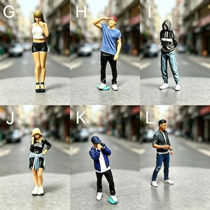 Puede incluir: Figuras en miniatura de personas en varias poses, incluyendo una mujer con top blanco y shorts negros, un hombre en monopatín y una persona con sudadera con capucha. Las figuras están situadas sobre un fondo borroso de calle.