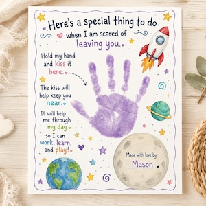 Puede incluir: Una impresión rectangular blanca con una huella de mano morada en el centro, rodeada de ilustraciones con temática espacial que incluyen un cohete, un planeta con anillos, la Tierra y estrellas. El texto dice: Here's a special thing to do when I am scared of leaving you. Hold my hand and kiss it here. The kiss will help keep you near. It will help me through my day so I can work, learn, and play! Made with love by: Mason.