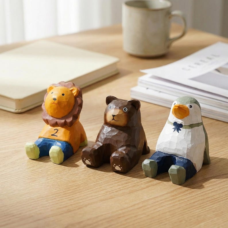 May include: Three wooden animal figurines: a lion with the number 2 on its shirt, a brown bear, and a penguin. The lion has an orange mane and shirt, blue pants, and green feet. The bear is brown, and the penguin has a white shirt, blue pants, and a blue bow tie.