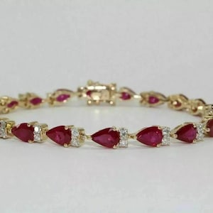 May include: A gold link bracelet featuring a repeating pattern of pear-shaped red rubies alternating with small, clear, round-cut diamonds. The jewelry piece is connected by a secure metal clasp mechanism, showcasing a consistent design throughout.