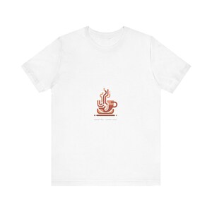 May include: White t-shirt featuring a minimalist coffee cup design in shades of brown, with steam rising above. The text "SERIOUS FIRST - COFFEE LATER" is printed below the graphic. A casual tee for coffee lovers.