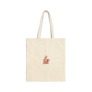 May include: Cream-colored tote bag with a brown coffee cup and steam graphic. The bag has long handles and is made of a sturdy fabric. The coffee cup graphic is centered on the front of the bag.