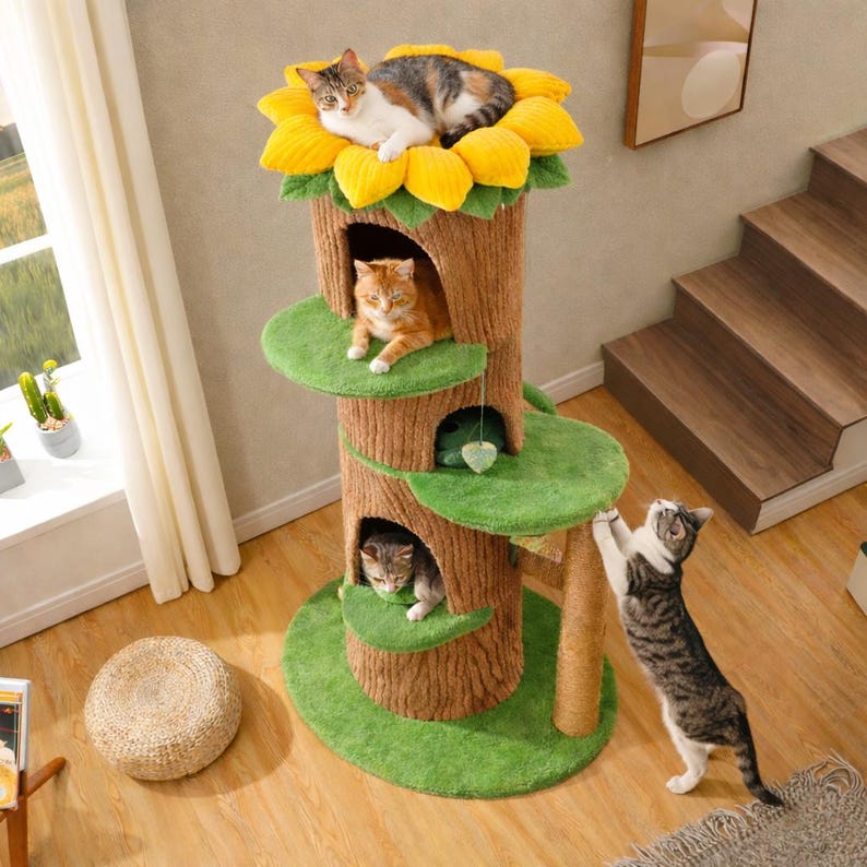 May include: A multi-level cat tree with a sunflower-shaped top, tree trunk design, and green platforms. Three cats are lounging on the tree. One cat is climbing the side. The tree has a natural, textured appearance.