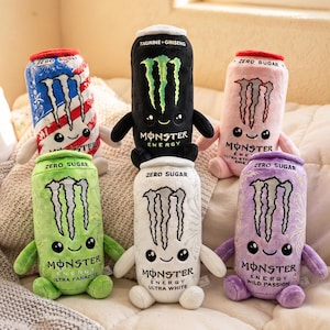 Può includere: Sei peluche a forma di lattine di bevande energetiche, ognuno con un viso sorridente, braccia piccole e gambe. Le lattine sono blu con strisce rosse e bianche, nere, rosa, verdi, bianche e viola, tutte con il logo Monster Energy.
