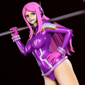 May include: A figurine of a character with pink hair and purple attire, holding a metal staff. The figure wears a form-fitting purple bodysuit with white accents, pink gloves, and a headset. The letters "VP" are visible on the chest.