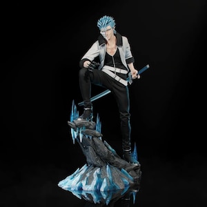 Puede incluir: Figura detallada de un personaje con pelo azul puntiagudo, que lleva una chaqueta blanca, pantalones negros y empuña una espada. La figura posa sobre una base rocosa con detalles de cristal azul, sobre un fondo negro.