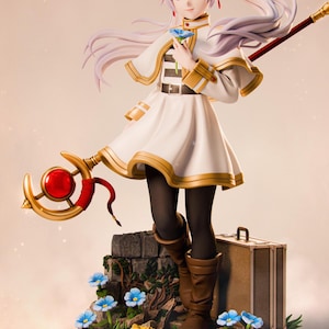 May include: A detailed figurine of a female character with long, flowing white hair, wearing a white dress with gold trim and black tights. She holds a blue flower and a staff with a red orb. The figure stands on a base with flowers and a suitcase.