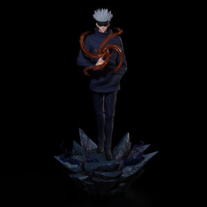 Op de afbeelding: Gedetailleerd beeldje van een personage uit de anime-serie Jujutsu Kaisen. Het beeldje draagt een donkerblauwe outfit, een blinddoek en stekelig wit haar. Een wervelend oranje energie-effect omringt het beeldje. Het beeldje staat op een rotsachtige basis.