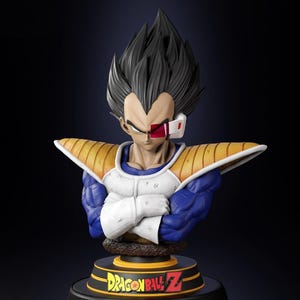 May include: A bust of the character Vegeta from Dragon Ball Z. The figure has spiky black hair, a stern expression, and is wearing armor with blue, white, and gold accents. The base features the Dragon Ball Z logo.