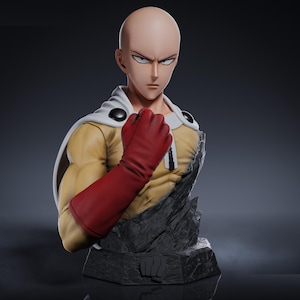 Puede incluir: Busto detallado del personaje de anime Saitama de One-Punch Man. La figura presenta una cabeza calva, expresión severa, mono amarillo, guantes rojos y capa blanca. La base es un diseño rocoso y gris.