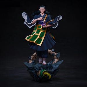 以下が含まれることがあります： 呪術廻戦のキャラクターの精巧なフィギュア。濃い青色のローブに金と緑のアクセント、渦巻く紫色のオーブを持っています。岩の台座の上に立ち、下からモンスターが現れています。