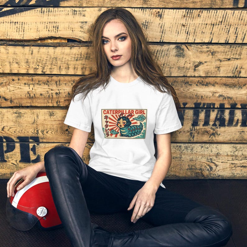 May include: White t-shirt featuring a colorful graphic of a caterpillar girl with Japanese text. The design includes a red sun, blue clouds, and a vintage aesthetic. The shirt is paired with black pants.