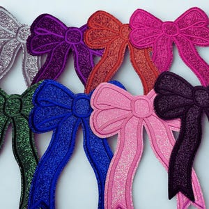 Peut inclure: Collection d'arcs en tissu pailleté de différentes couleurs : argent, violet, rouge, rose, vert, bleu et noir. Chaque nœud présente un design détaillé avec de longues queues fluides, parfait pour l'artisanat ou la décoration.