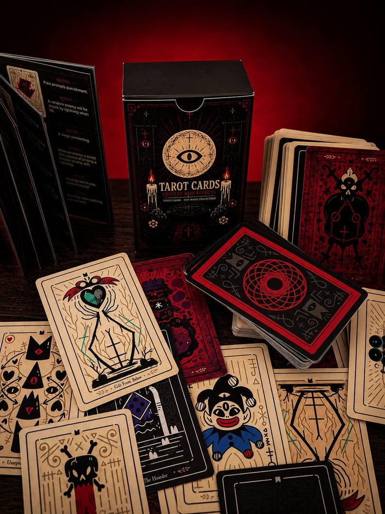 May include: A deck of tarot cards featuring a black box with an eye graphic and the text Tarot Cards Quotes and Effects. The cards display various illustrations including a jester, a skull, and abstract symbols in red, black, and cream colors.