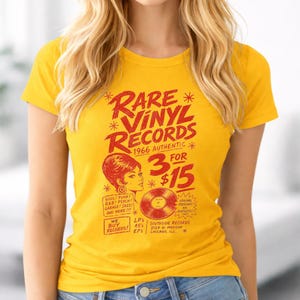 May include: Mustard yellow t-shirt featuring a vintage design for "Rare Vinyl Records." The red graphic includes text, a woman's silhouette, and a record illustration. The shirt promotes records from 1966, with a price of 3 for £15.