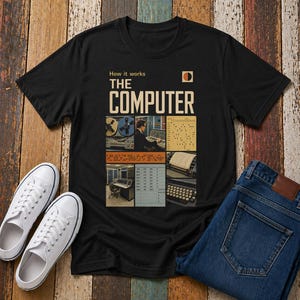 May include: Black t-shirt with the text "THE COMPUTER" and images of vintage computer equipment. The shirt also features the text "How it works". White canvas trainers and blue jeans are next to the shirt.