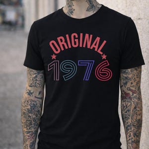 Könnte beinhalten: Schwarzes T-Shirt mit dem Wort "ORIGINAL" in Rot und der Zahl "1976" in Blau und Rot. Das Design enthält zwei Sterne. Das Shirt hat einen Rundhalsausschnitt.