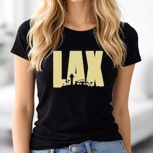 May include: Black t-shirt with the gold text "LAX". The design shows a silhouette of the Los Angeles International Airport, including palm trees and famous buildings. A casual, short-sleeved tee.