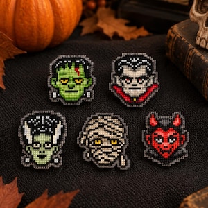 May include: Five pixel art style embroidered patches featuring classic monster characters: a green Frankenstein's monster, a vampire with a red cape, a green bride of Frankenstein, a beige mummy wrapped in bandages, and a red devil with horns.