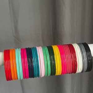 May include: A collection of thin, smooth bangles arranged in a row, featuring a vibrant spectrum of colours including red, orange, turquoise, hot pink, navy blue, light pink, green, dark green, yellow, magenta, crimson, white, grey, and black.