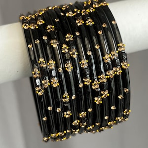 May include: A set of ten glossy black bangles arranged in a row. Each bangle features a series of small, sparkling champagne-coloured rhinestones set in clusters against the dark surface, creating a repetitive pattern across the entire collection.