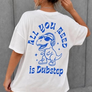 May include: A white short-sleeved t-shirt featuring a blue graphic on the back. The design depicts a Tyrannosaurus Rex wearing sunglasses and headphones, surrounded by small stars, with the text "ALL YOU NEED is Dubstep" in blue.