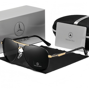 May include: Black aviator sunglasses with gold detailing, a black case, and a white box. The sunglasses and packaging feature the Mercedes-Benz logo. The case and box are branded with the Mercedes-Benz logo.