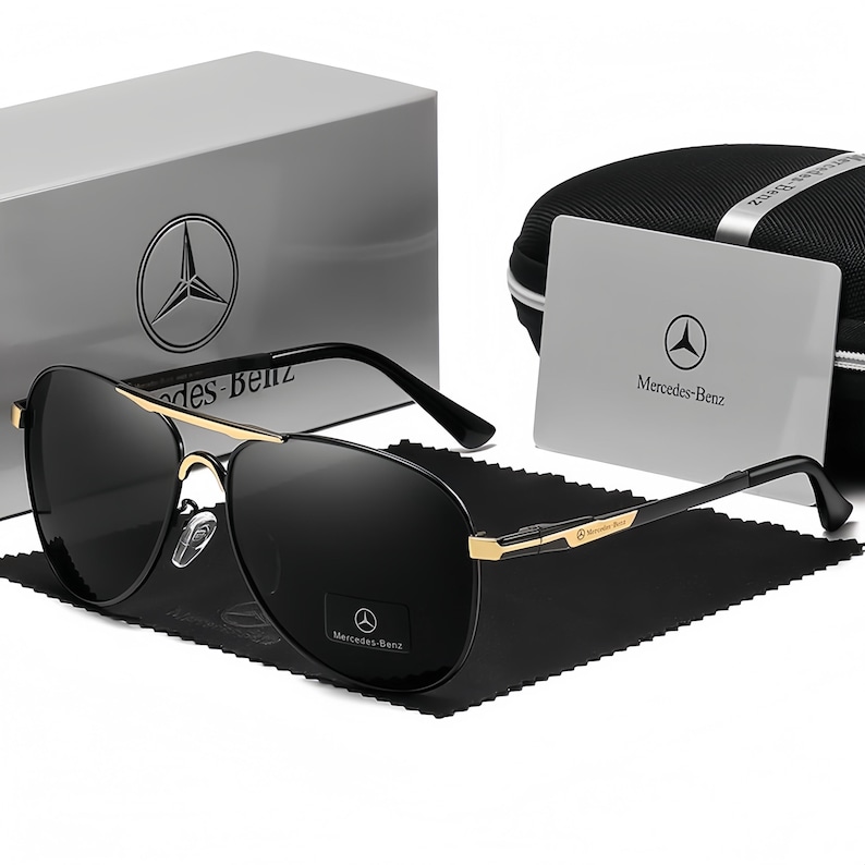 May include: Black aviator sunglasses with gold detailing, a black case, and a white box. The sunglasses and packaging feature the Mercedes-Benz logo. The case and box are branded with the Mercedes-Benz logo.