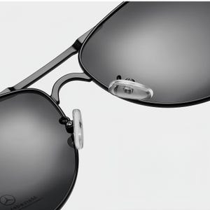 May include: Close-up of black sunglasses with a metal frame and dark lenses. The sunglasses have a classic aviator style with clear nose pads. The lenses reflect the light, and the frame appears to be matte black.