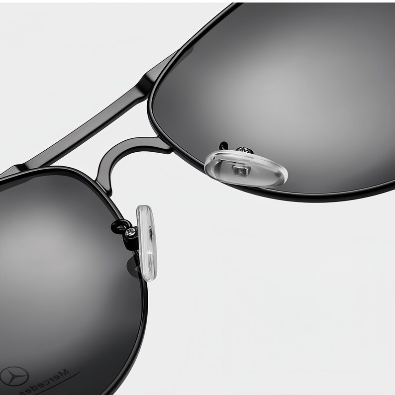 May include: Close-up of black sunglasses with a metal frame and dark lenses. The sunglasses have a classic aviator style with clear nose pads. The lenses reflect the light, and the frame appears to be matte black.
