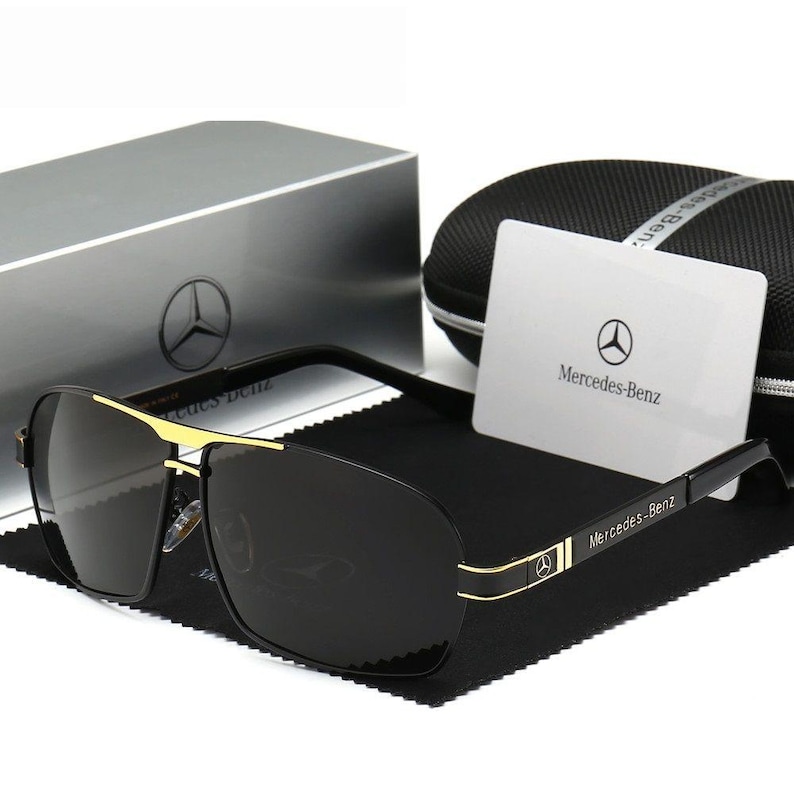 May include: Black sunglasses with gold detailing and the Mercedes-Benz logo on the frame and card. The sunglasses are presented with a case and box, both featuring the Mercedes-Benz emblem.