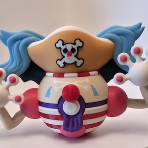 May include: A 3D printed figure of a clown character with blue hair, a tan pirate hat featuring a skull and crossbones emblem, and a round body with red and white horizontal stripes. The figure has white hands with pink fingertips and a purple tongue.