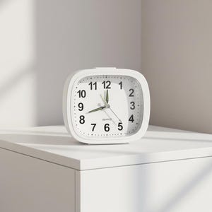 May include: A white quartz alarm clock with a square face and rounded corners. The clock face has black numerals, a second hand, and two other hands. The clock is sitting on a white surface.