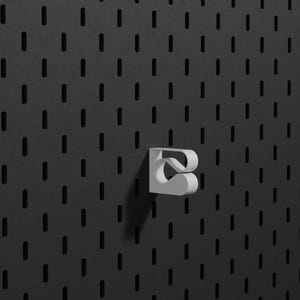 May include: A white, three-dimensional hook with a curved, stylised shape attached to a dark grey pegboard. The pegboard features a repeating pattern of vertical, rounded rectangular slots arranged in a grid across the entire surface.